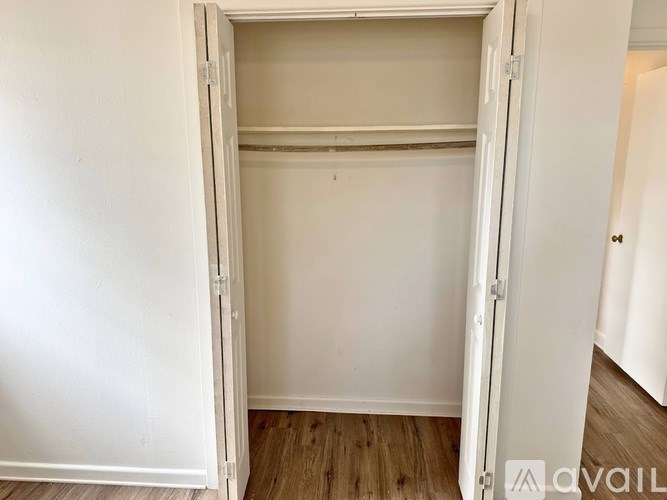 A white open closet with a wooden floor.
