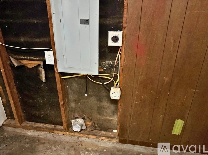 A dirty basement with a white door and a white electrical box on the wall.