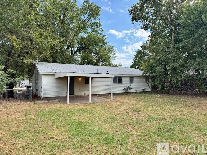 A white garage with a metal roof is surrounded by trees and grass.