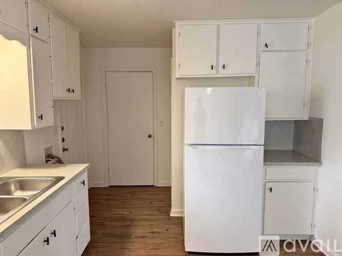 A white kitchen with a fridge, sink and cabinets.