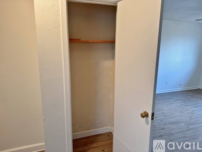 A white door with a gold handle is open to a room with a white wall and a wooden floor.