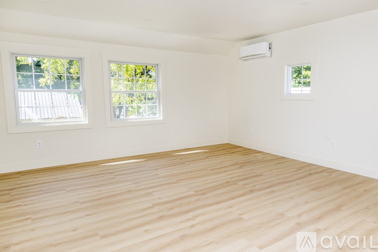 A room with wooden flooring and two windows.