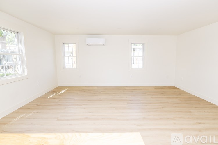 A room with wooden flooring and two windows.