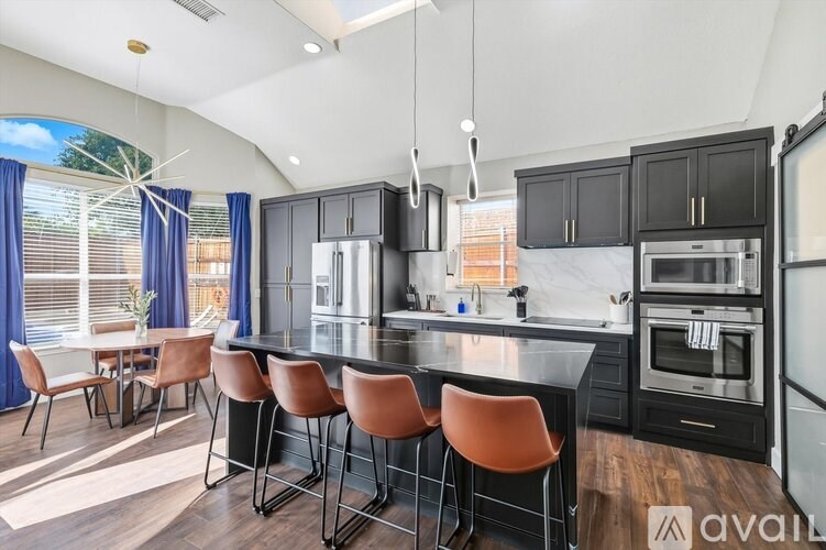A kitchen with black cabinets and a long island with four chairs.
