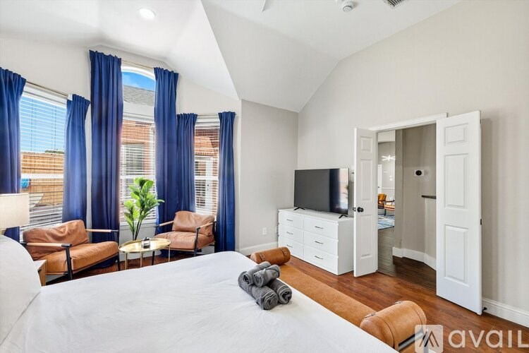 A bedroom with a large bed, a television, and a window with blue curtains.