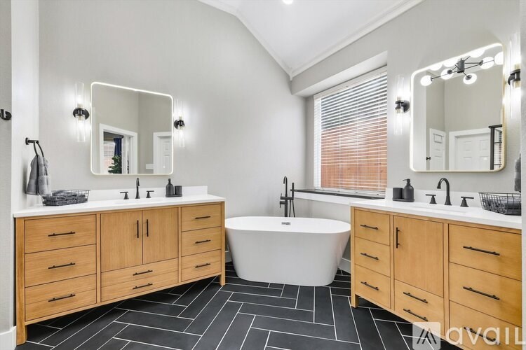 A modern bathroom with a white tub, wooden cabinets, and a large mirror.