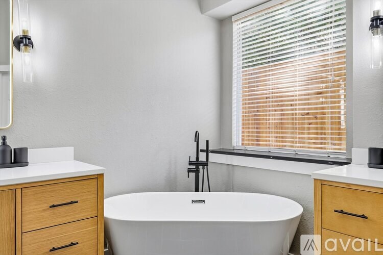 A bathroom with a white tub, wooden cabinets, and a window with blinds.