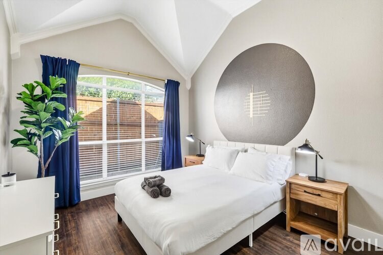 A bedroom with a large bed, a wooden nightstand, and a plant in a vase.