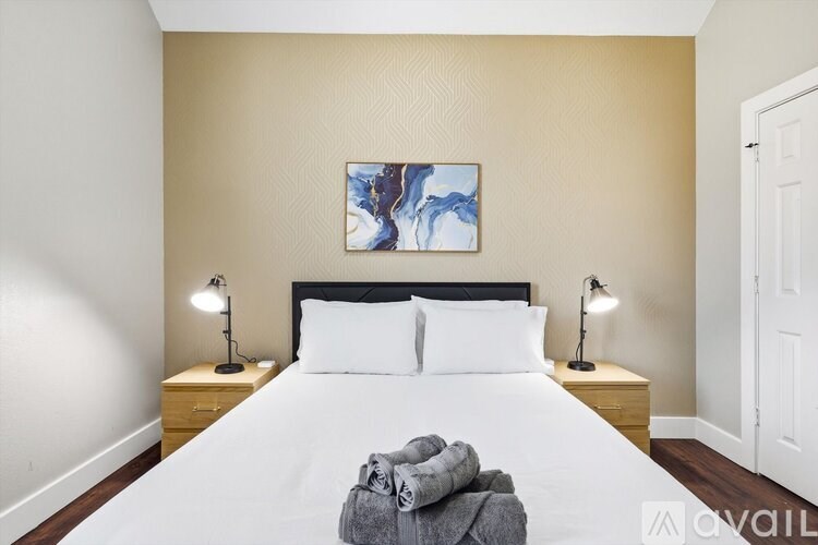 A bedroom with a large bed, two lamps, and a painting on the wall.