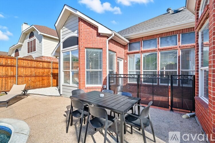 A patio with a table and chairs is surrounded by a fence and a brick building.