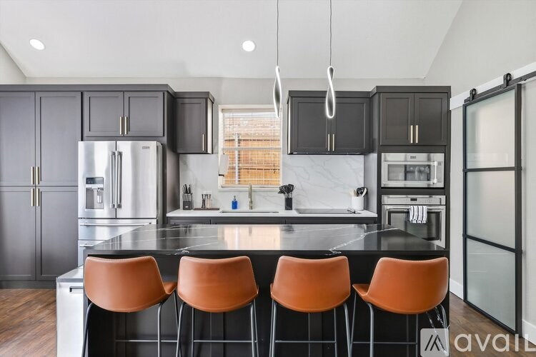 A kitchen with black cabinets and orange chairs.