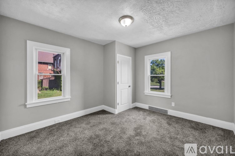 A room with a carpeted floor, a door, and a window showing a view of a house.