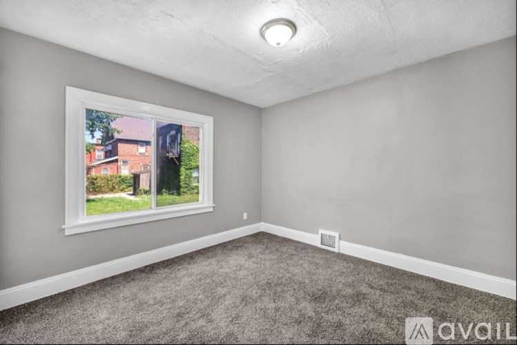 A room with a window showing a view of a house and trees.