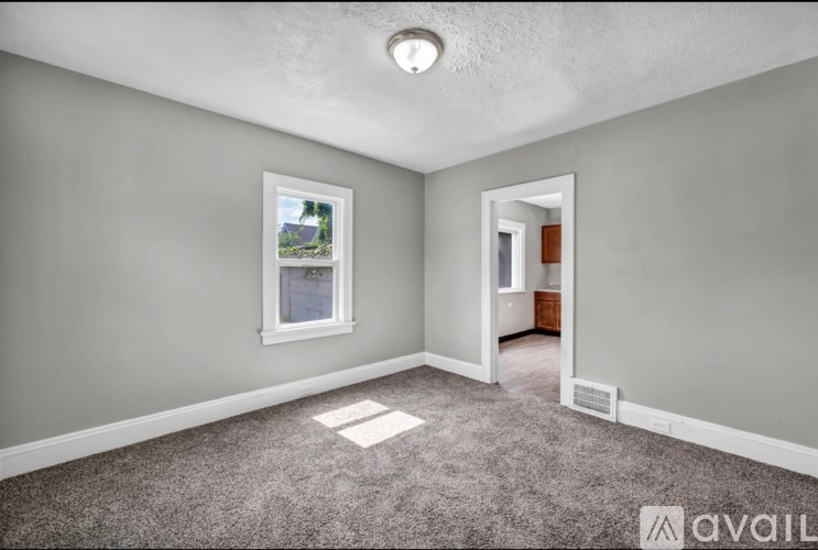 A room with a carpeted floor, a window, and a door leading to another room.