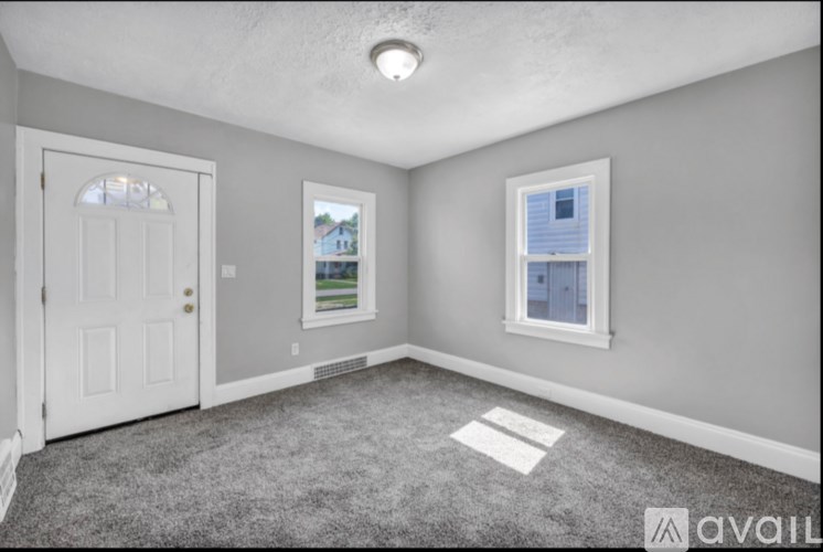 A room with a carpeted floor, a door, and a window with a view of a house across the way.