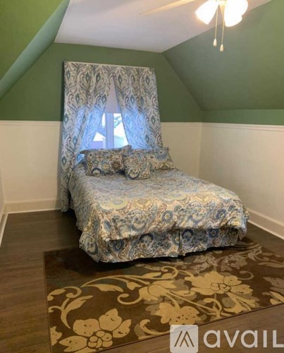 A bed with a blue and white patterned comforter sits on a patterned rug in a room with green walls.