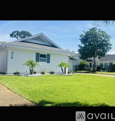 A white house with green lawn and trees in front.