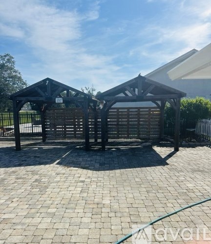A wooden gazebo with a roof is situated in a paved courtyard.
