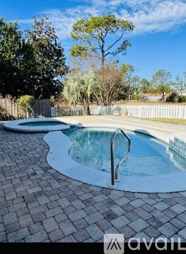 A pool surrounded by a brick patio and a white fence.