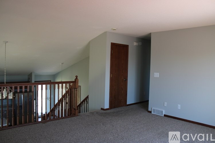 A room with a carpeted floor, a staircase with a railing, and a door.
