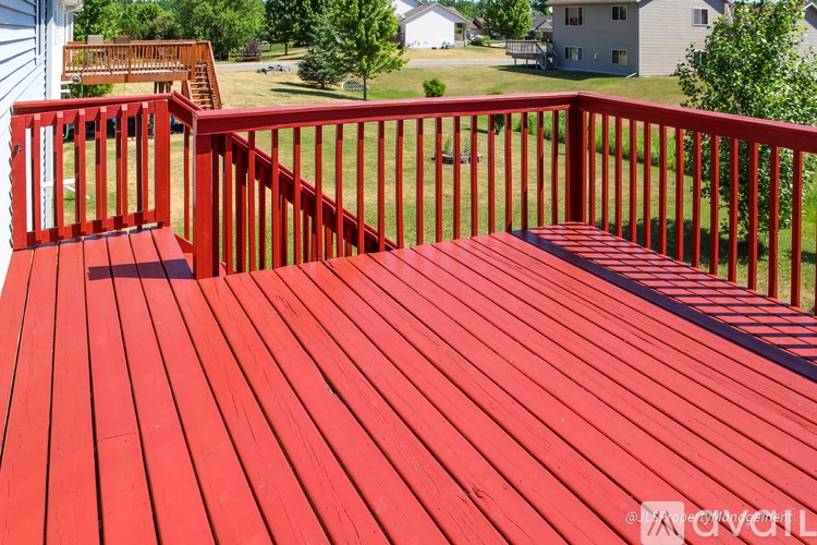 A red wooden deck with a bench and railings.