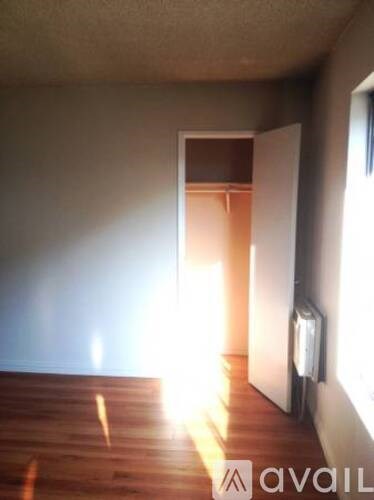 A room with a wooden floor and a white wall with a doorway leading to another room.