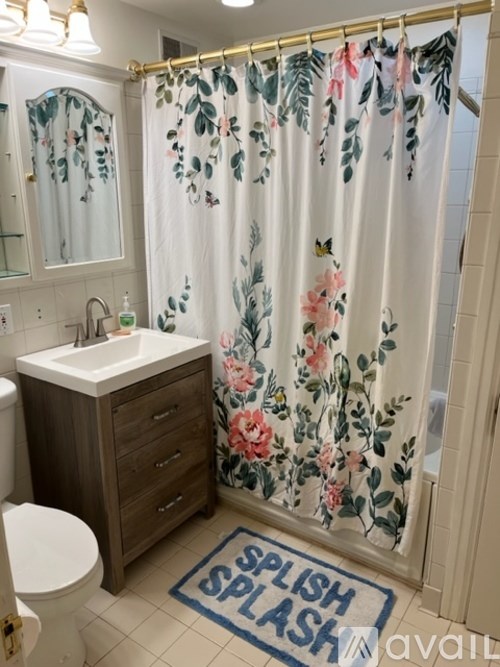 A bathroom with a floral shower curtain and a rug that says "Splish Splash".