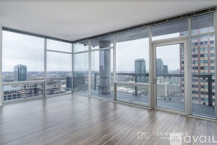 A spacious room with wooden floors and large windows overlooking a cityscape.