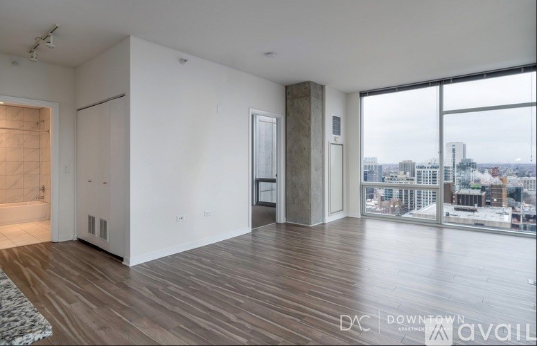 A spacious room with wooden floors and a view of the city through large windows.