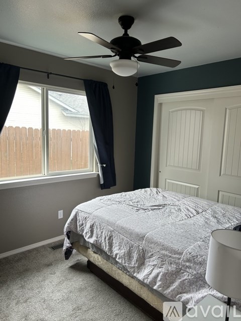 A bedroom with a bed, a ceiling fan, and a window with a view of a fence.