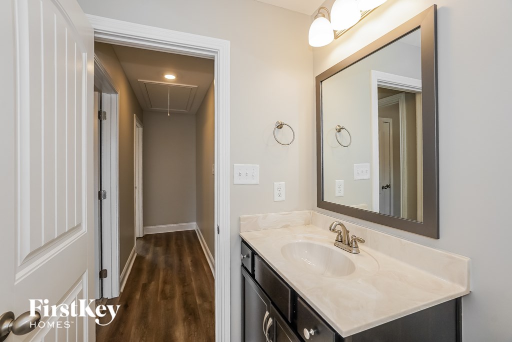 A bathroom with a sink, mirror, and wooden floors.