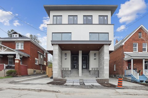 A modern house with a white facade is in front of older brick houses.