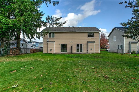A house with a grey roof and a brown siding is surrounded by a green lawn.