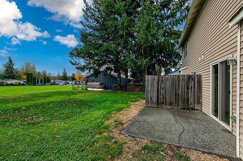 A house with a brown siding and a grey door is surrounded by a green lawn and trees.