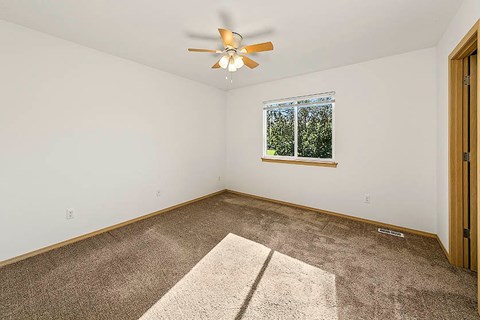 A room with a ceiling fan and a window with a view of trees.