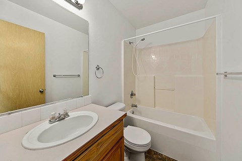 A white sink with a wooden cabinet and a white toilet in a bathroom.