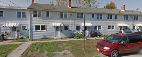 A red car is parked in front of a grey building.
