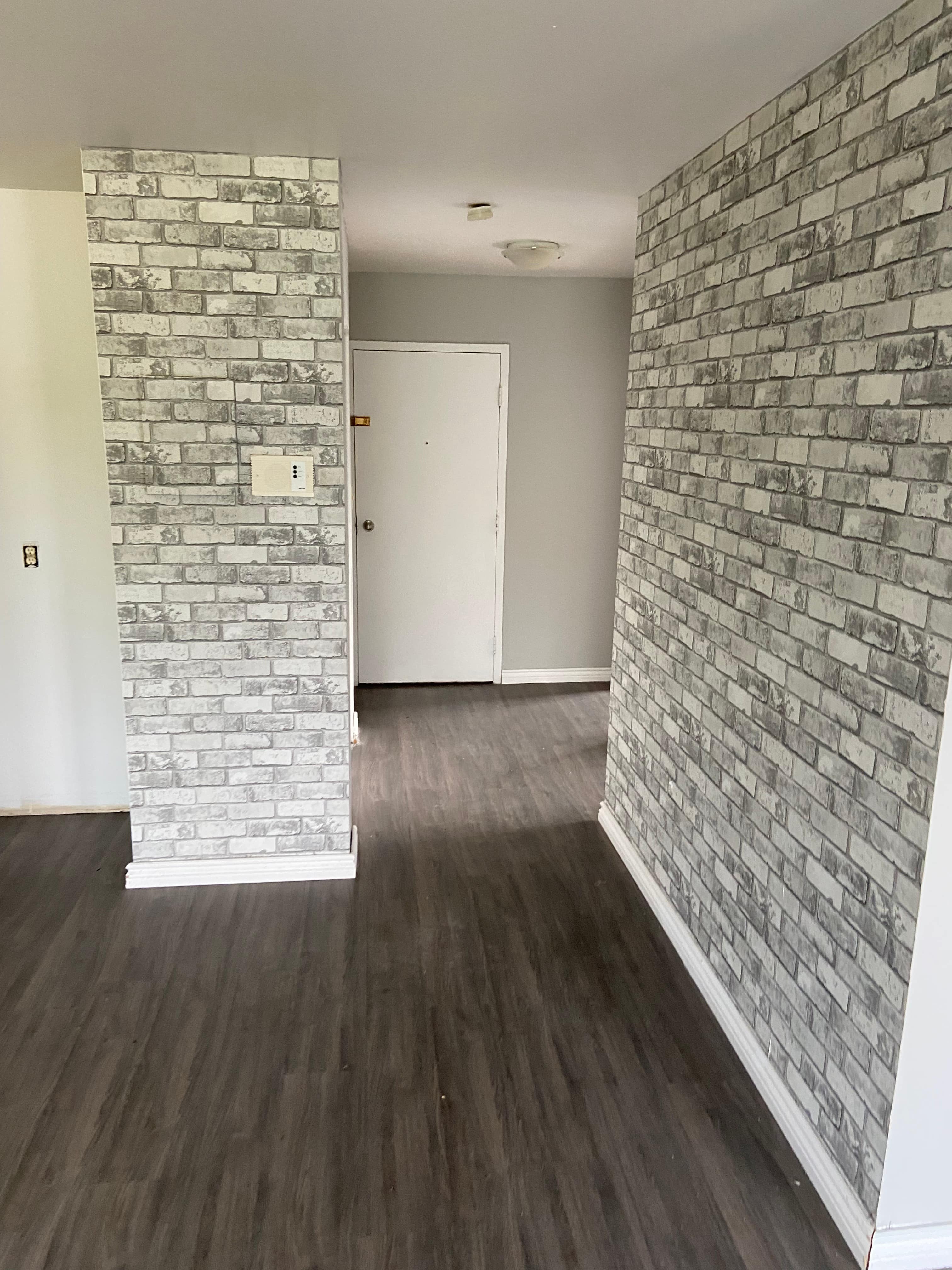 A room with a white door and a brick wall.