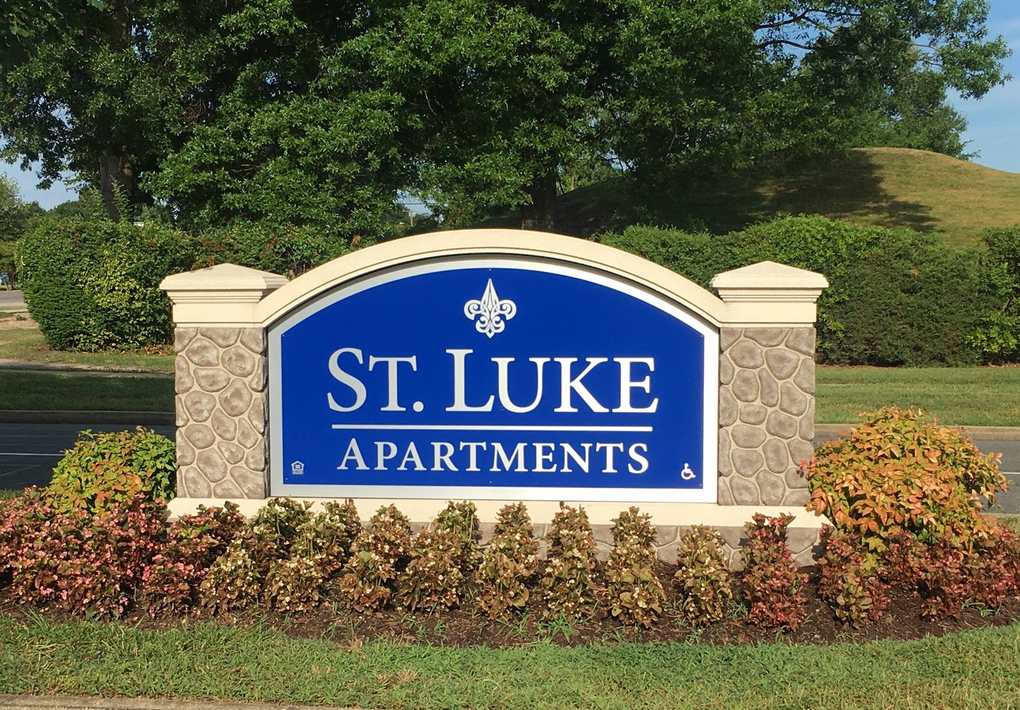 A sign for St. Luke Apartments is surrounded by shrubbery.