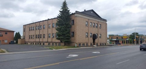 A large brick building with a black roof sits on the corner of a street.