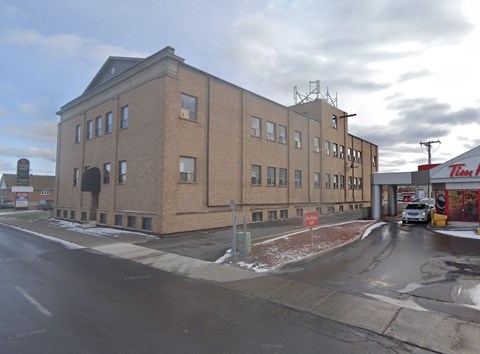 A large brick building with a flat roof and a parking lot in front.