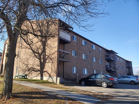 A black car is parked on the side of a road in front of a brick building.