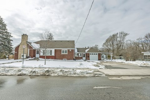 A red brick building with a white door and a chimney is surrounded by snow.