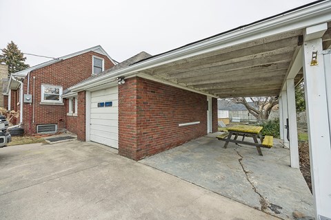 A brick house with a white garage door and a picnic table under a covered porch.