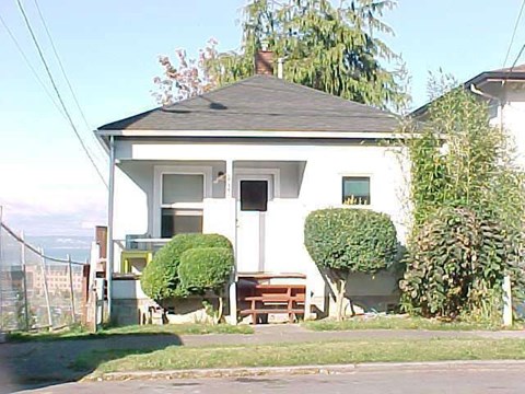 A white house with a black roof and a tree in front of it.