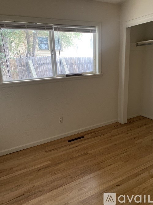 A room with wooden flooring and a window overlooking a fence.