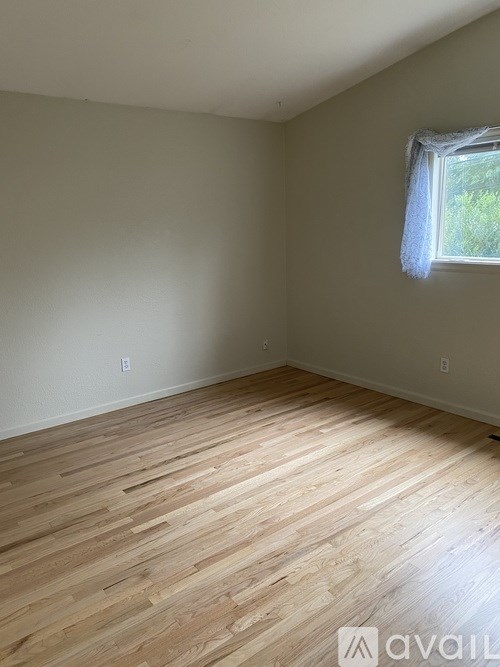 A room with wooden flooring and a window with a white curtain.