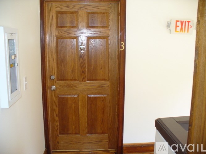 A wooden door with a glass window on the left and a red exit sign on the wall.