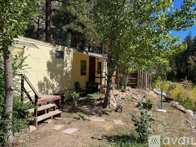 A small yellow house surrounded by trees and plants.
