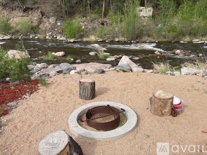 A fire pit sits in the middle of a sandy area with a river and trees in the background.